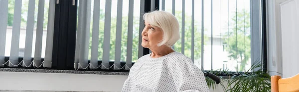 Mujer mayor mirando hacia otro lado en la sala del hospital, pancarta - foto de stock