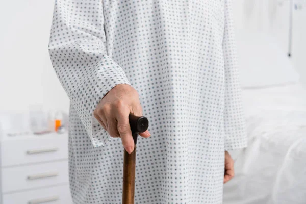 Vista recortada de una anciana sosteniendo bastón en la sala de hospital - foto de stock