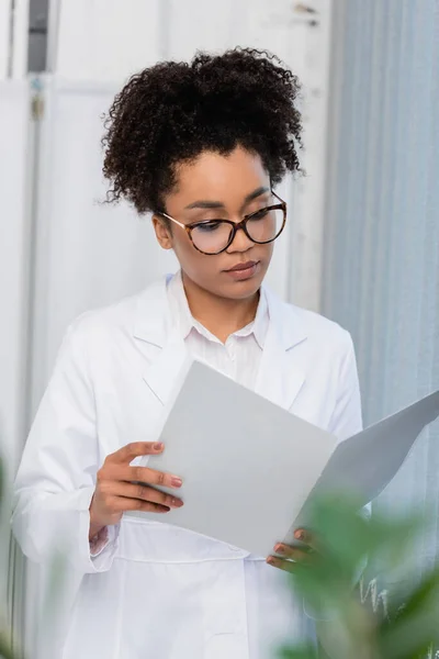 Médecin afro-américain en lunettes regardant le dossier papier — Photo de stock
