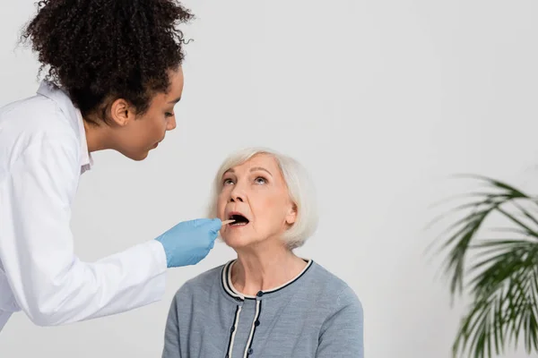 Лікар - американець у латексі перевіряє горло старшого пацієнта. — стокове фото