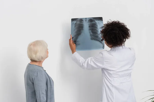 African american doctor holding fluorography near patient and wall in clinic — Stock Photo