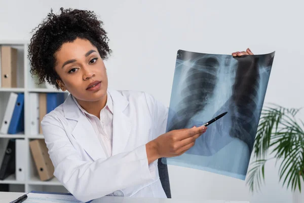 African american doctor pointing at fluorography while looking at camera — Stock Photo