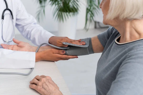 Vista recortada del médico afroamericano usando tonómetro en la mujer en el hospital - foto de stock