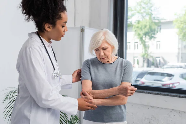 Африканский американец-травматолог, стоящий возле пожилой женщины, касающейся руки — стоковое фото