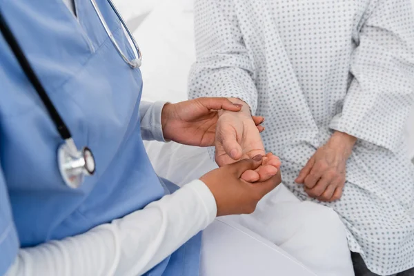 Vista recortada de la enfermera afroamericana comprobando el pulso en la mano del paciente mayor - foto de stock