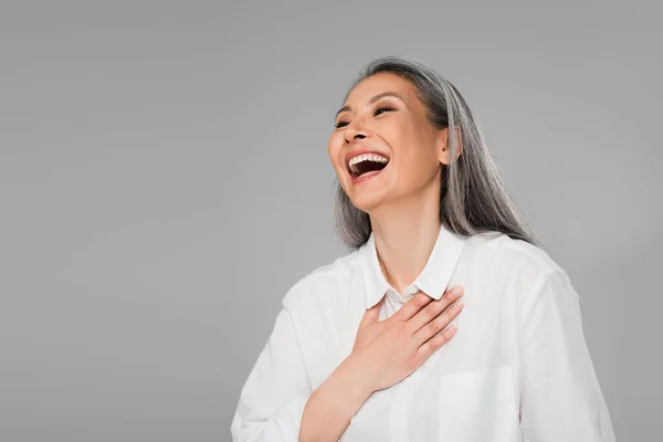 Sobrejoyed asiático mujer con gris pelo tocando pecho mientras risa aislado en gris - foto de stock