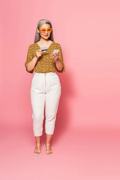 Вид в полный рост трогательной женщины с кредитной картой и мобильным телефоном в розовом цвете — стоковое фото