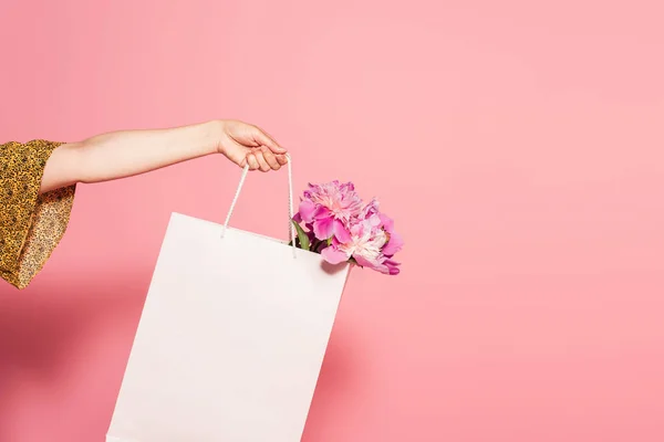 Vista parziale della donna con peonie fresche in shopping bag su sfondo rosa — Foto stock