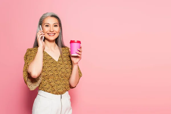 Satisfeito asiático mulher com takeaway bebida chamando no celular no rosa fundo — Fotografia de Stock
