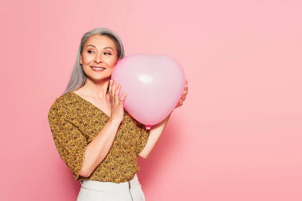Feliz asiático mujer en patrón blusa celebración de corazón en forma de globo en rosa fondo - foto de stock