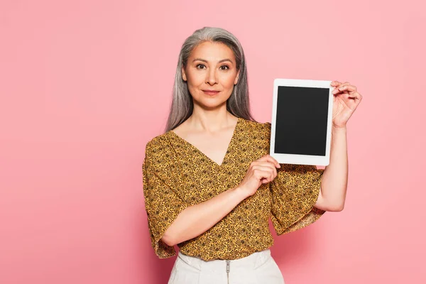 Reife asiatische Frau zeigt digitale Tablette mit leerem Bildschirm auf rosa Hintergrund — Stockfoto