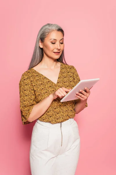 Femme asiatique à la mode en utilisant une tablette numérique tout en se tenant sur fond rose — Photo de stock