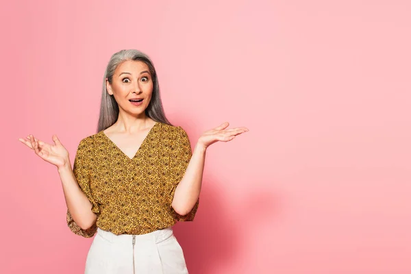 Amazed asian woman with open mouth pointing with hand on pink background — Stock Photo