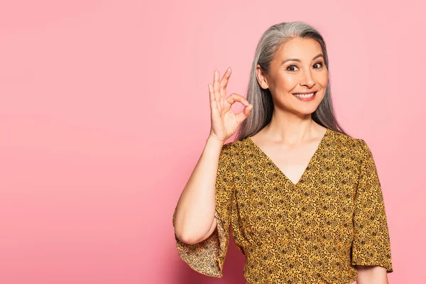 Happy asian woman in yellow blouse with pattern showing okay gesture on pink background — Stock Photo