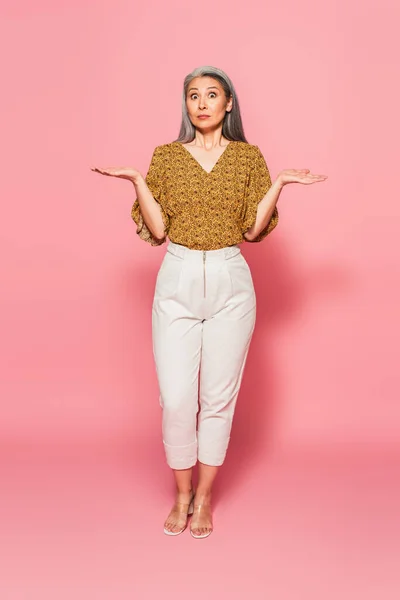 Full length view of shocked asian woman pointing with hands on pink background — Stock Photo