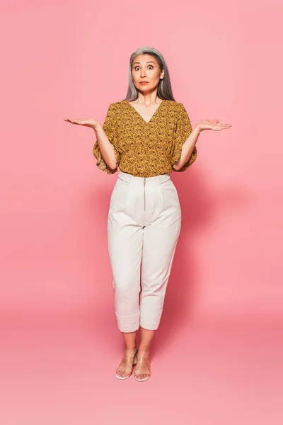 Longitud completa vista de conmocionado asiático mujer apuntando con las manos en rosa fondo - foto de stock