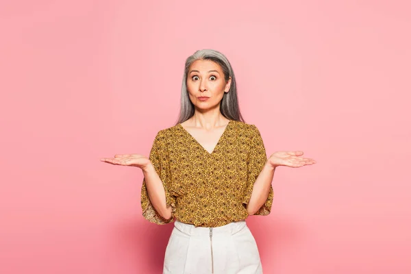 Discouraged asian woman pointing with hands while looking at camera on pink — Stock Photo