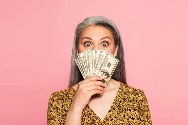 Amazed asian woman covering face with dollar banknotes isolated on pink — Stock Photo