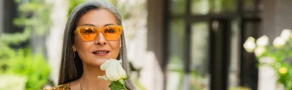 Donna matura asiatica in occhiali da sole gialli con rosa bianca all'aperto, banner — Foto stock