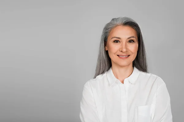 Joyful asian woman in white shirt smiling at camera isolated on grey — Stock Photo