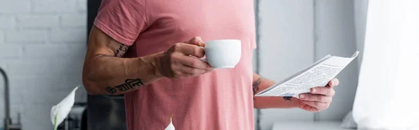 Cropped view of man holding newspaper and coffee at home, banner — Stock Photo