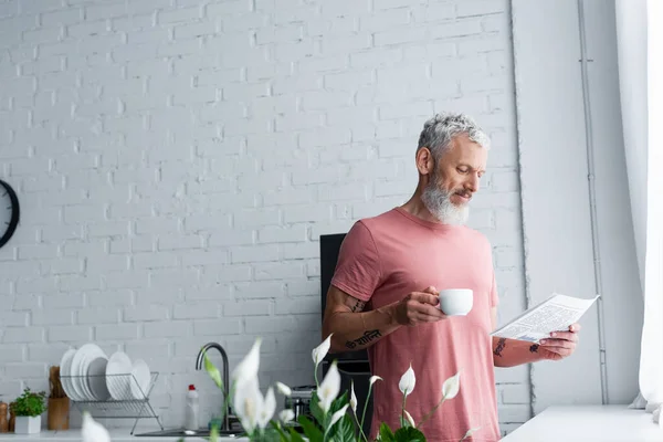 Mature man with coffee reading news in kitchen — Stock Photo