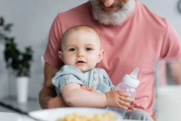 Babymädchen mit Flasche blickt in Kamera neben Vater — Stockfoto