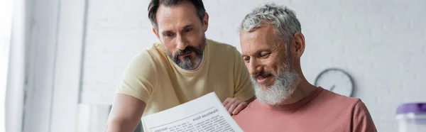 Улыбающийся гомосексуалист читает новости рядом с партнером дома, баннер — стоковое фото