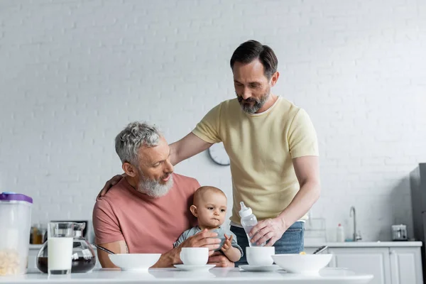 Homosexual couple holding baby bottle near daughter during breakfast — Stock Photo