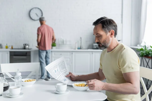 Homossexual homem ler notícias perto do café da manhã e parceiro borrado na cozinha — Fotografia de Stock