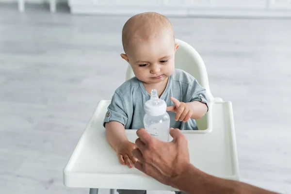 Отец держит бутылку с водой рядом с ребенком на стульчике — стоковое фото