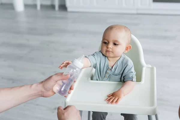 Bottiglia per bambini con acqua vicino al bambino sul seggiolone — Foto stock