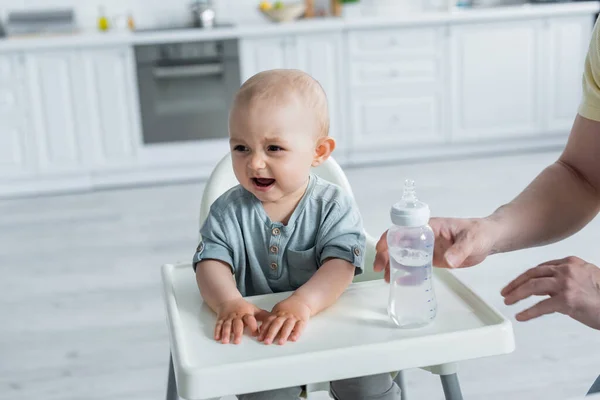 Filha bebê chorando perto de pai e garrafa na cadeira alta — Fotografia de Stock