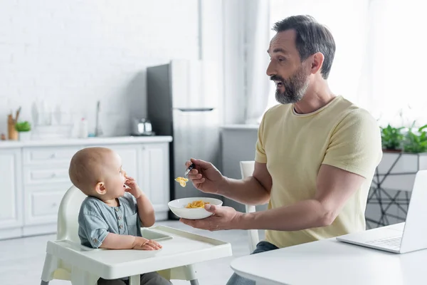 Vista laterale del padre maturo che tiene i fiocchi di mais vicino alla figlia sul seggiolone — Foto stock