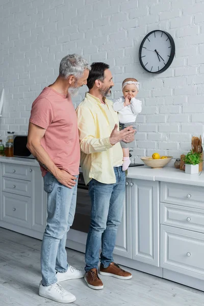 Усміхнений батько тримає доньку неподалік від партнера на кухні — стокове фото