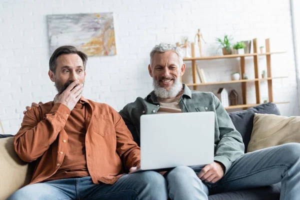 Lächelnder homosexueller Mann benutzt Laptop neben erstaunter Partnerin — Stockfoto