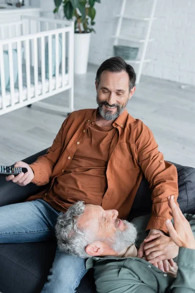 Sorridente uomo omosessuale che tiene la mano del partner e telecomando — Foto stock