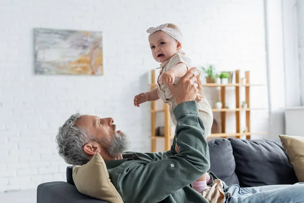 Mature father holding crying baby on couch — Stock Photo