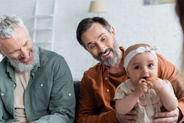 Lächelnde gleichgeschlechtliche Eltern, die ihr Baby im Wohnzimmer betrachten — Stockfoto