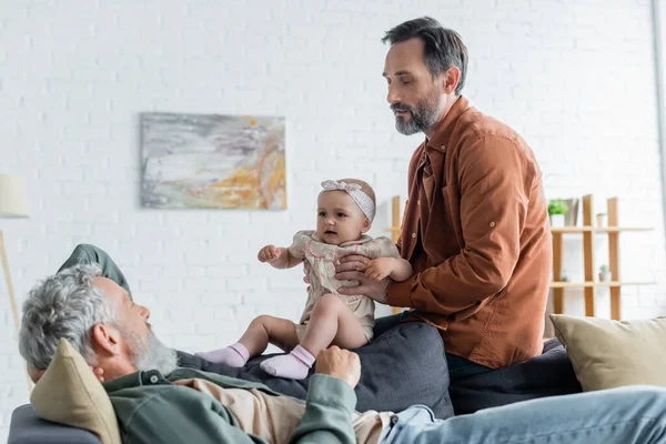 Homosexual parents holding toddler daughter on couch — Stock Photo