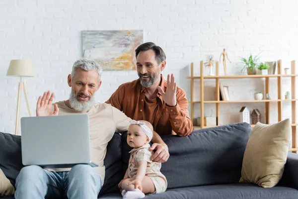 Homosexual couple waving hands during video call near daughter at home — Stock Photo