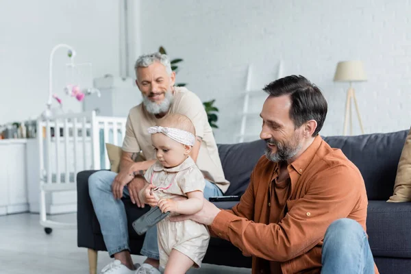 Homosexual father holding toddler kid near smiling partner on blurred background — Stock Photo