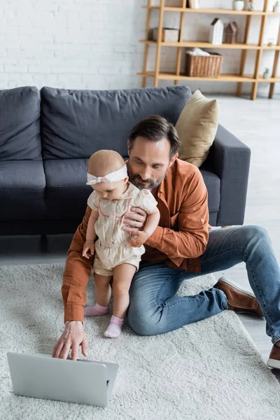 Man using laptop and holding toddler daughter on carpet — Stock Photo