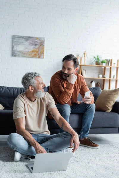 Homosexual couple with smartphone and laptop in living room — Stock Photo