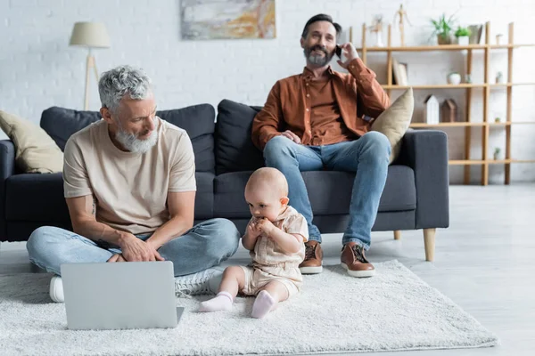 Toddler child sitting near homosexual father with laptop on carpet — Stock Photo