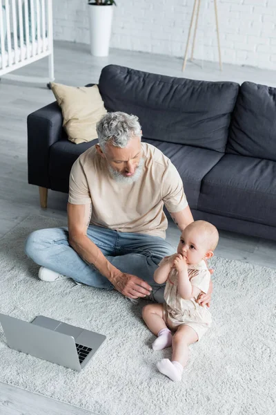 Vue grand angle de mature freelancer étreignant fille près d'un ordinateur portable sur le tapis — Photo de stock