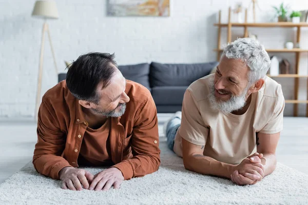 Cheerful homosexual couple looking at each other on carpet — Stock Photo