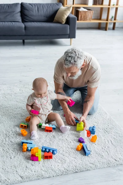 Высокий угол обзора малыша держа строительные блоки рядом с отцом на ковре — стоковое фото