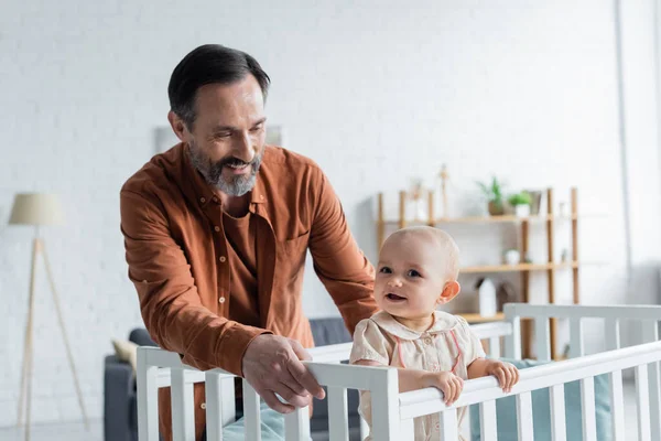 Smiling mature father looking at baby daughter in crib — Stock Photo