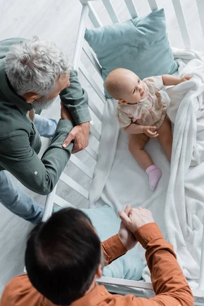 Visão geral de pais homossexuais olhando para a filha do bebê no berço — Fotografia de Stock